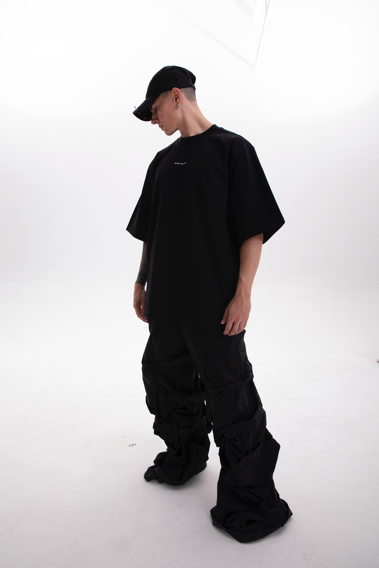 Model photographed from the right side wearing the Be Your Own God black heavyweight tee with minimal front print on a white background