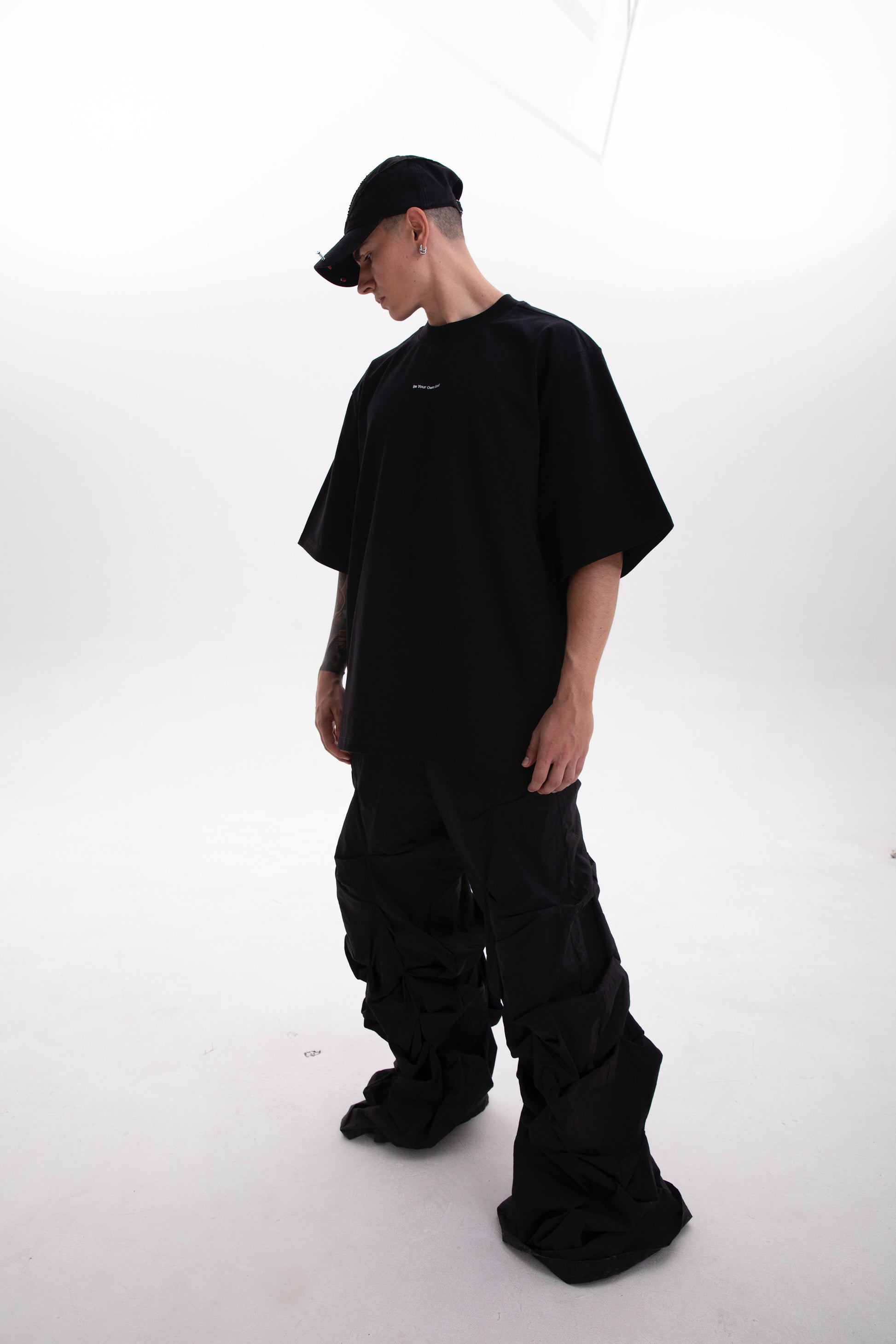 Model photographed from the right side wearing the Be Your Own God black heavyweight tee with minimal front print on a white background