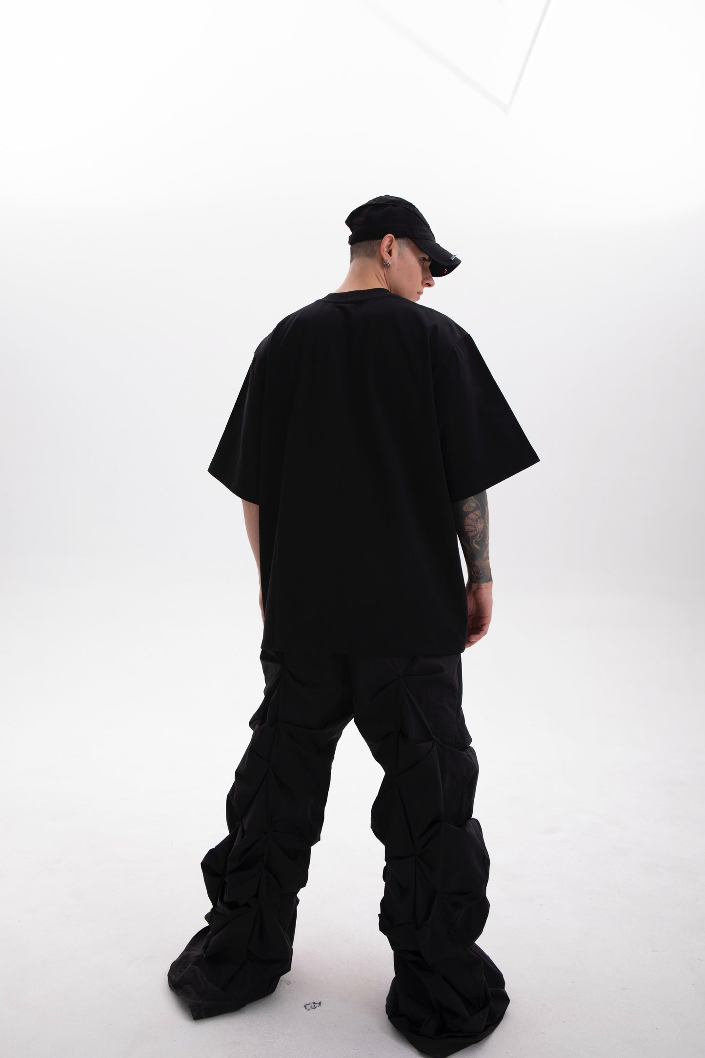 Model wearing the BYOG  black heavyweight t-shirt  photographed from the back side styled in dark aesthetic on a white background