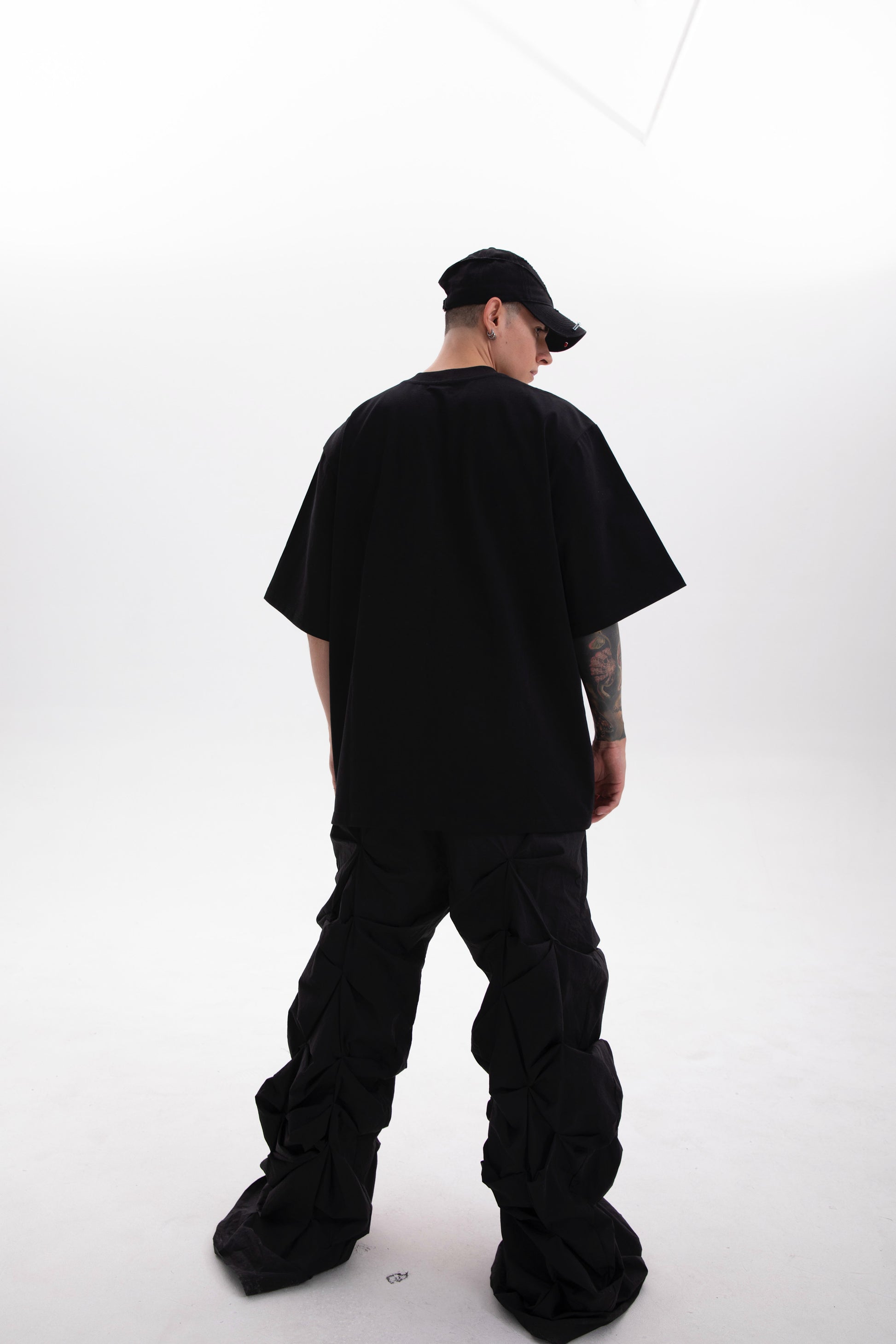 Model wearing the BYOG  black heavyweight t-shirt  photographed from the back side styled in dark aesthetic on a white background